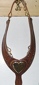 Leather horse breast collar with heart-shaped centerpiece hanging on a red wooden wall.