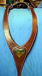 Leather horse breast collar with heart-shaped center piece. Brown leather, brass hardware, on blue fabric.