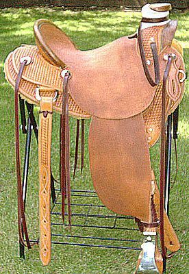 Brown leather western saddle on a black stand, in a grassy outdoor setting.