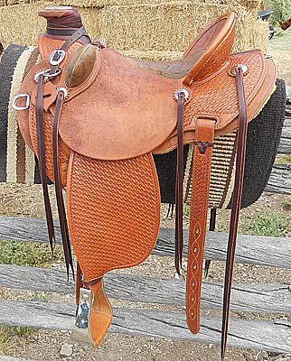 Leather western saddle on a wooden fence. Light brown with tooling details.