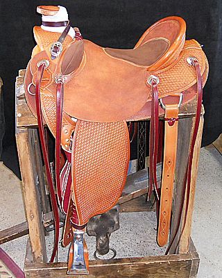 Tan leather Western saddle on a wooden stand; basketweave pattern on fenders, red accents.