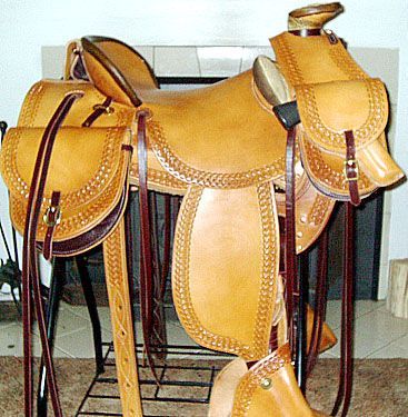 A tan leather western saddle with detailed tooling and saddlebags.