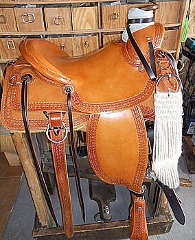 Tan leather western saddle with tooling detail, on wooden stand.