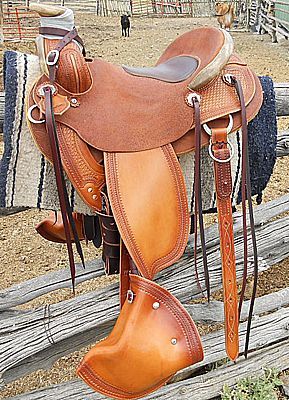 Brown leather western saddle hanging on a wooden fence, with a horse grazing in the background.