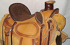 Close-up of a tan and brown leather horse saddle, with tooled designs and a dark brown seat.