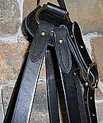 Close-up of black leather horse bridle with brass buckles and stitching, hanging against a brick wall.