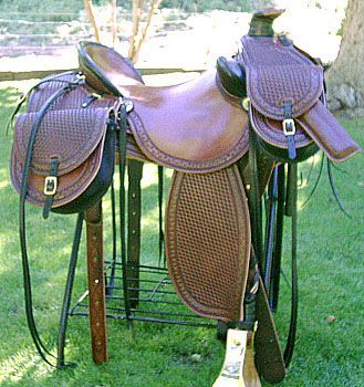Brown leather saddle on a metal stand, with attached saddlebags. Green grass background.
