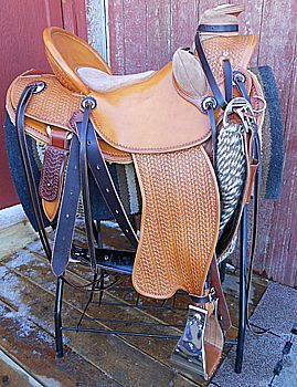 Tan leather western saddle on a black stand against a weathered red wooden wall.