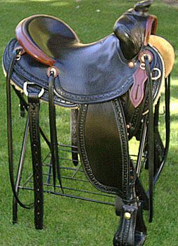 Black leather Western saddle on a stand, set outdoors on grass.