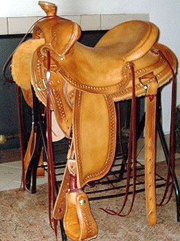 Brown leather western saddle on a black stand, detail of stitching and stirrups.