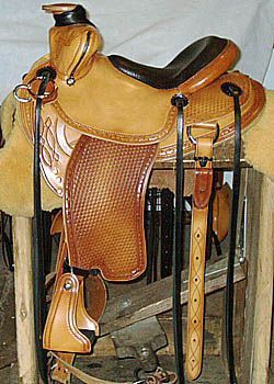 Tan and brown leather western saddle with detailed tooling, on a wooden stand.
