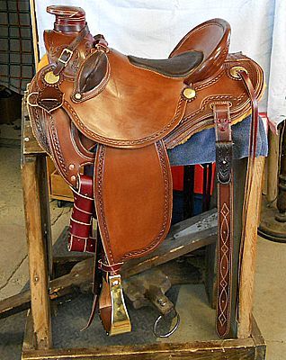Brown leather western saddle on a wooden stand with decorative stitching and brass details.