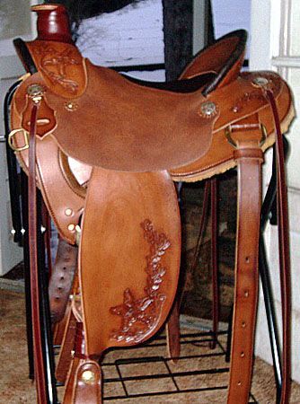 Brown leather Western saddle with floral tooling, displayed on a black stand.