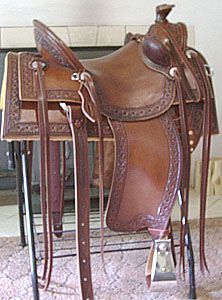 Brown leather Western saddle with decorative tooling, on a stand.