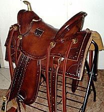 Brown leather western saddle on a black metal stand, with gold accents and leather straps.