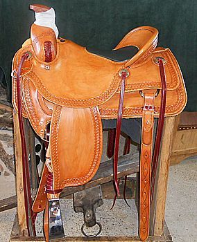 Tan leather western saddle on a wooden stand, with red accents and tooling details.