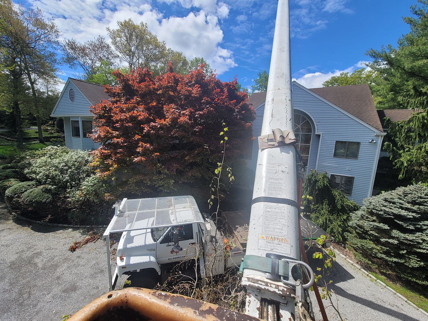 An old crane jib and rusted car frame in front of a white house with a red-leaved tree.
