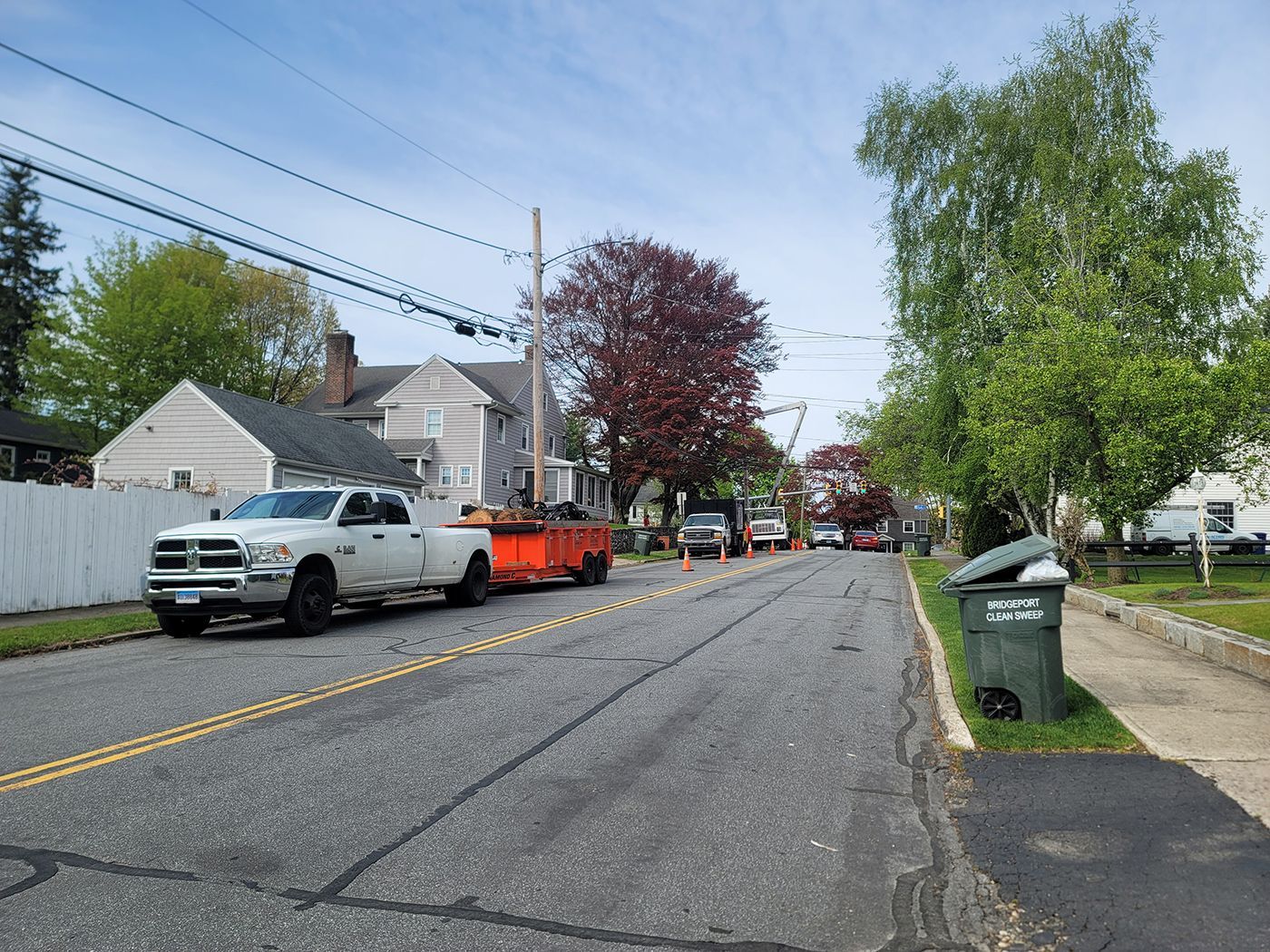 Street with utility trucks, cones, and trees; power lines above.
