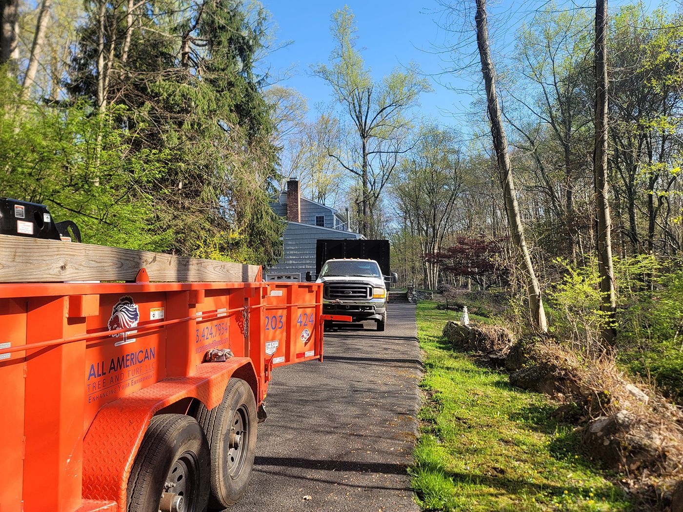 Orange trailer and truck parked on a driveway near a house; trees and greenery in the background.