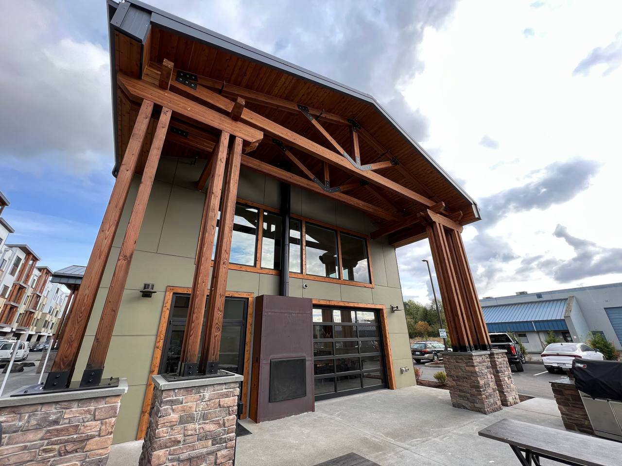 Modern building entrance with large wooden beams, stone accents, and glass windows under a cloudy sky