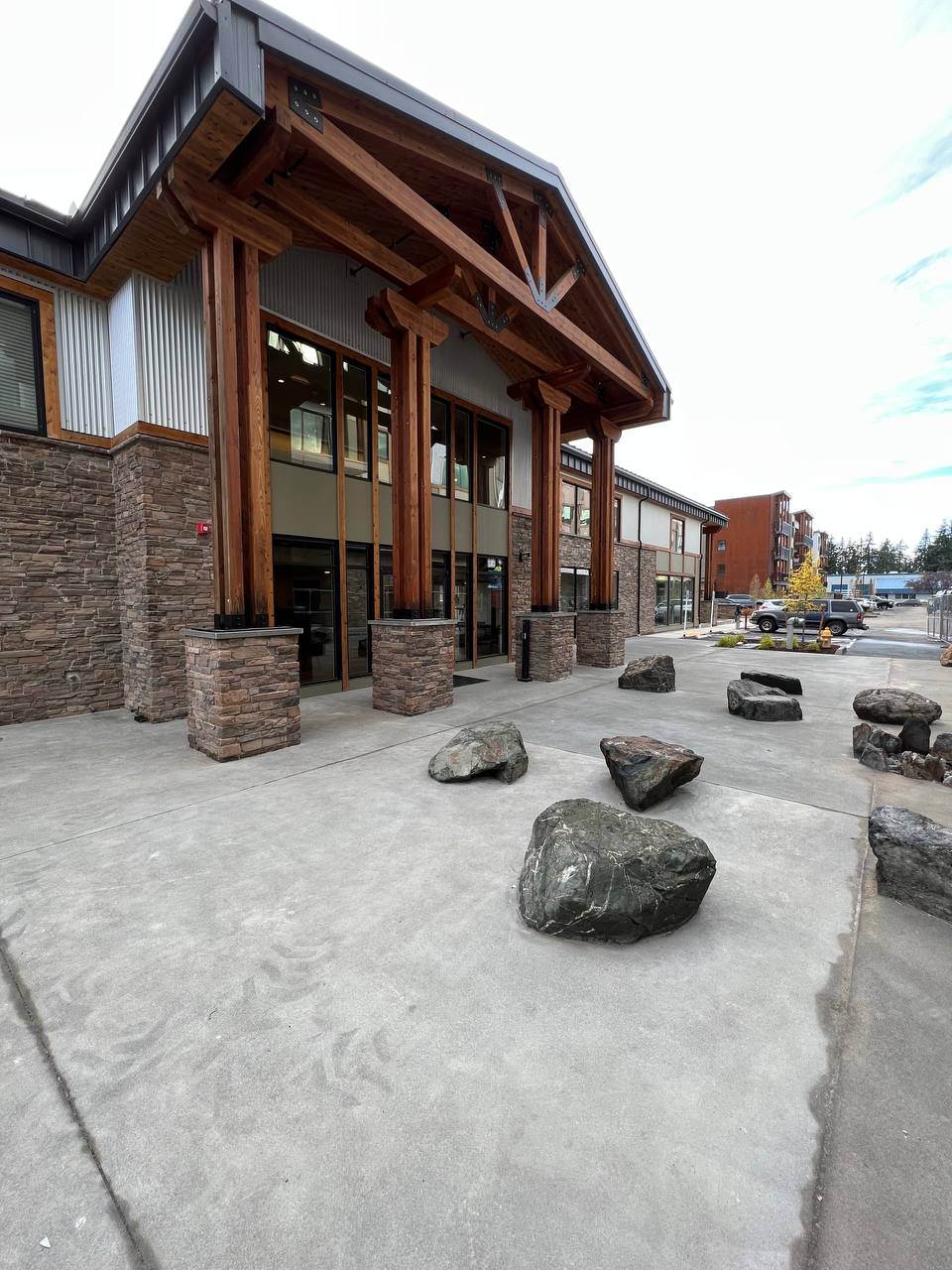 Stone-and-timber building entrance with large rocks on a concrete walkway, viewed from outside.