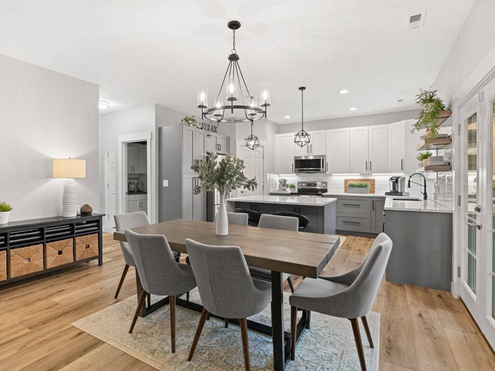 Modern open-plan dining room and kitchen with gray chairs, wood table, pendant lights, and white cabinets