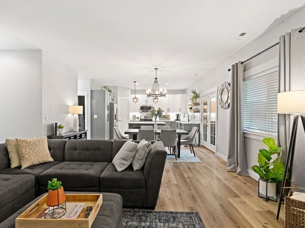 Bright open living room with dark sofa, wood floors, chandelier, and dining area beyond