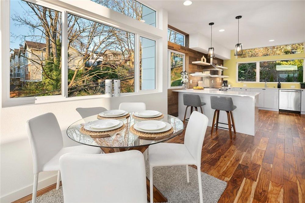 A dining room with a glass table and white chairs and a large window.