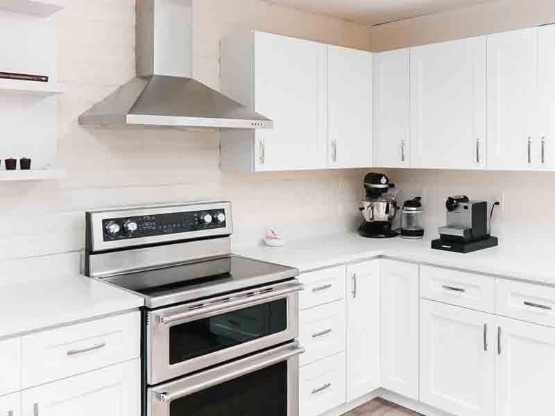 Bright white modern kitchen with stainless steel stove, range hood, and countertop appliances