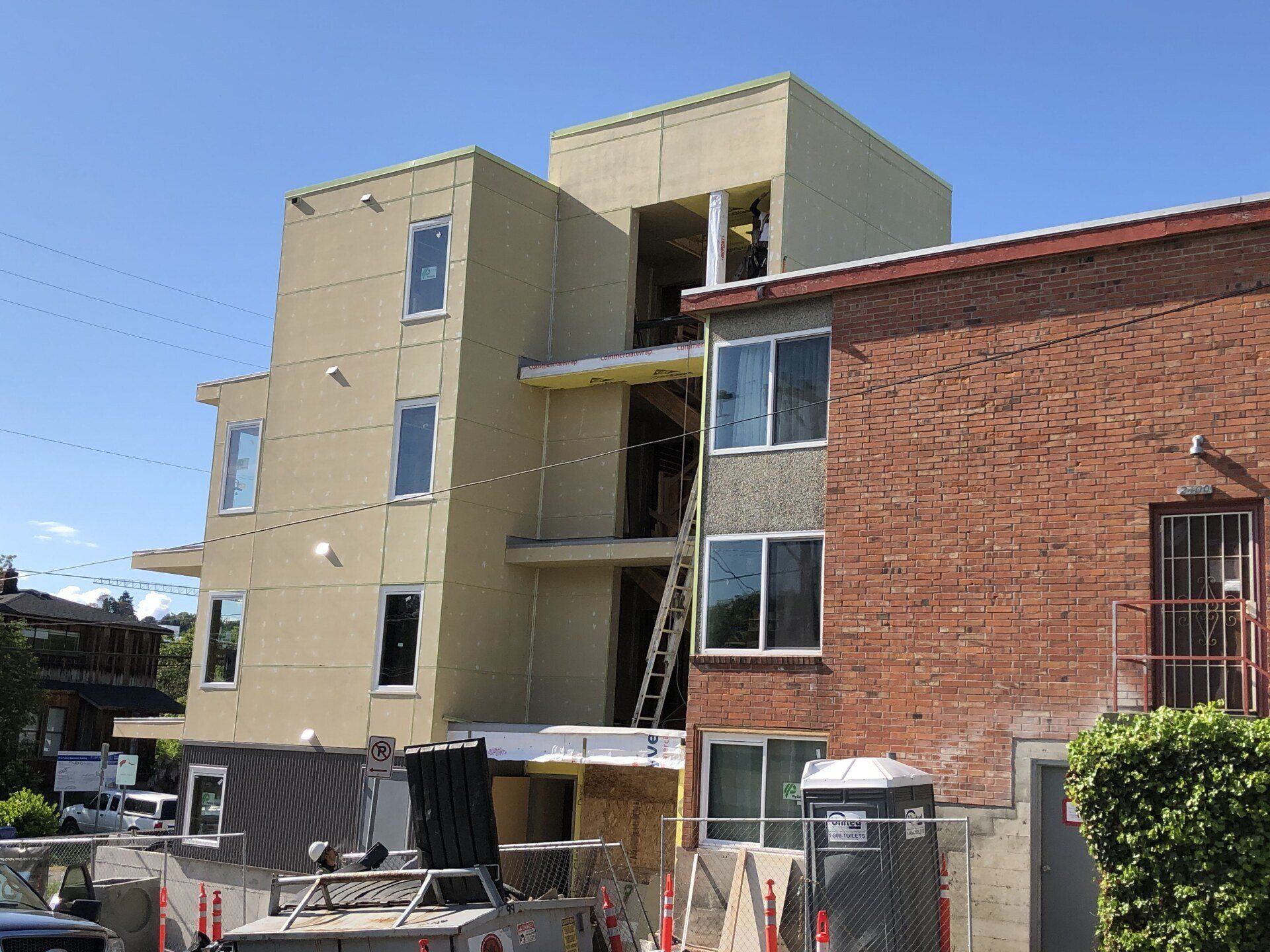 Modern beige apartment building beside a red brick house under a clear blue sky