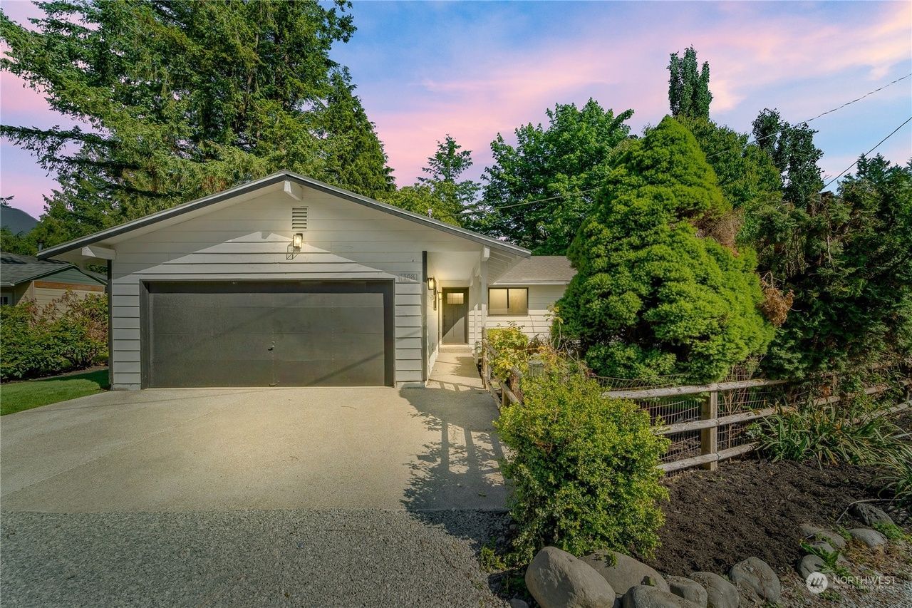 Suburban house with two-car garage, driveway, and lush front landscaping at sunset