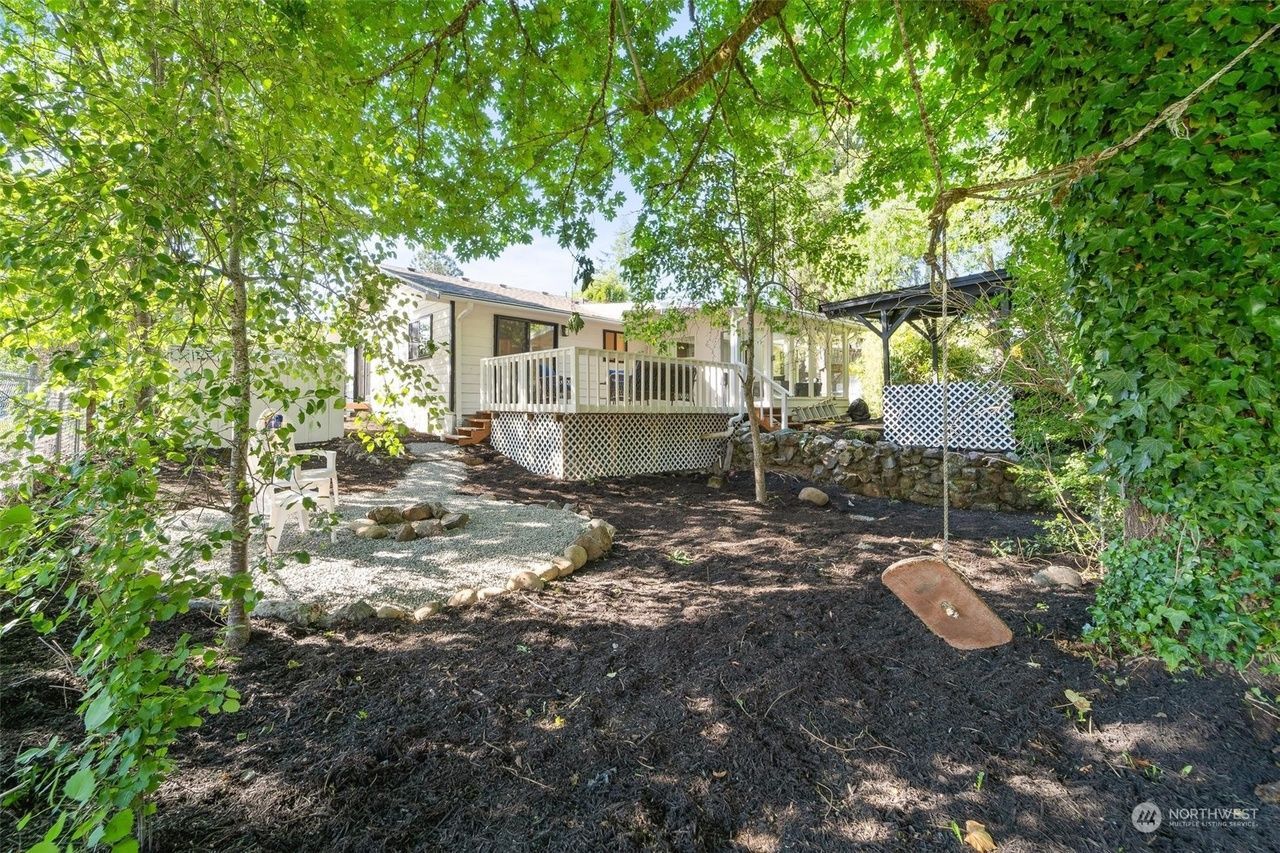 Shaded backyard with a white porch, gravel patio, and leafy trees surrounding a house
