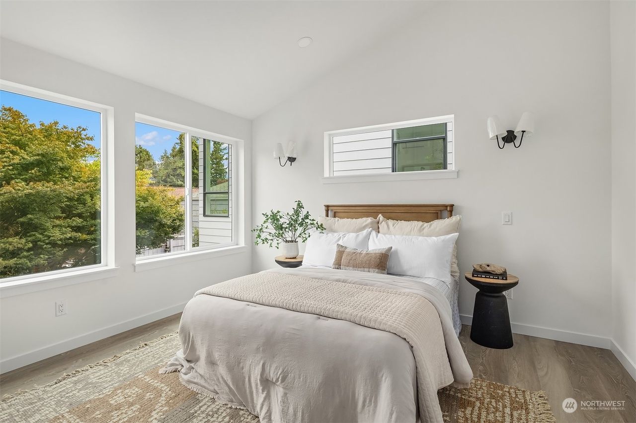 Bright minimalist bedroom with white walls, large windows, a bed, and a small plant on the nightstand