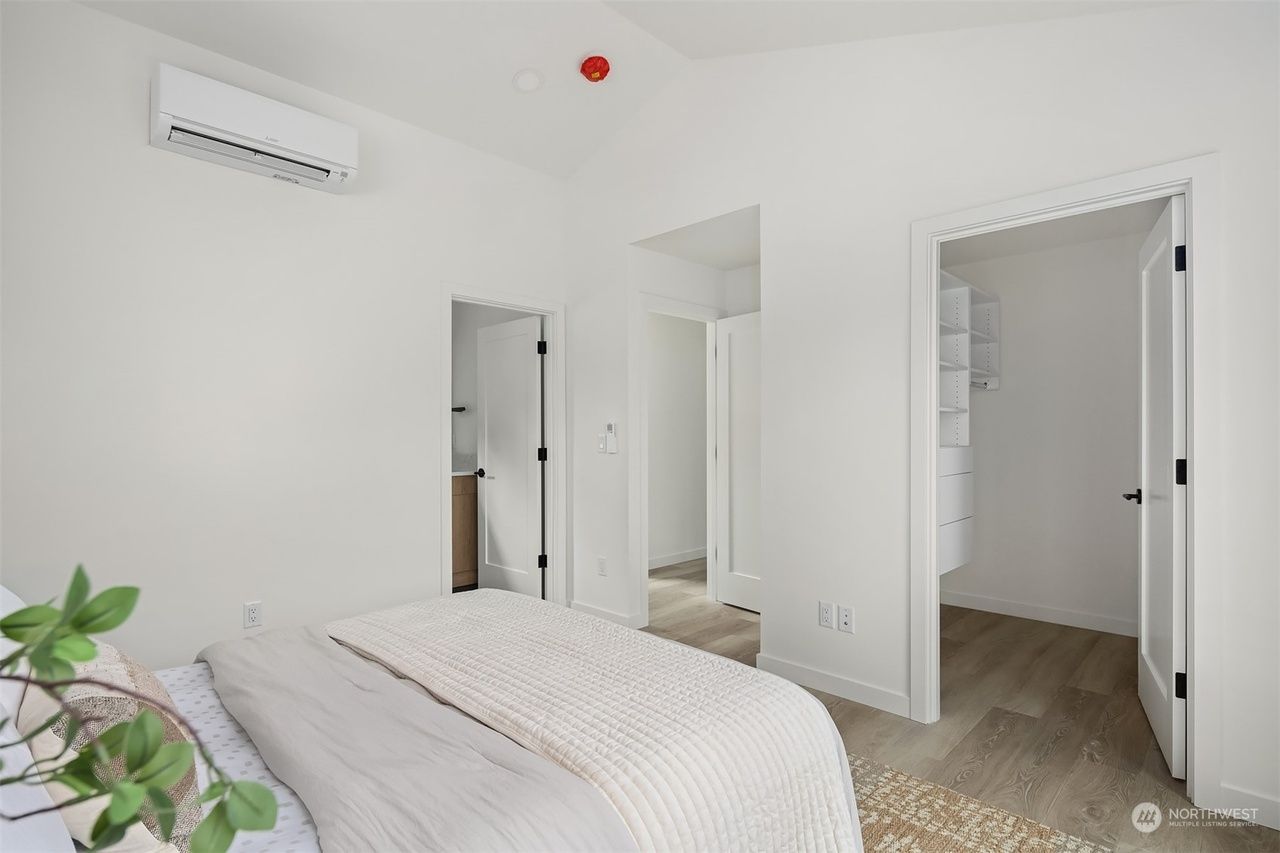Bright white bedroom with bed, closet, open door, and wall-mounted air conditioner