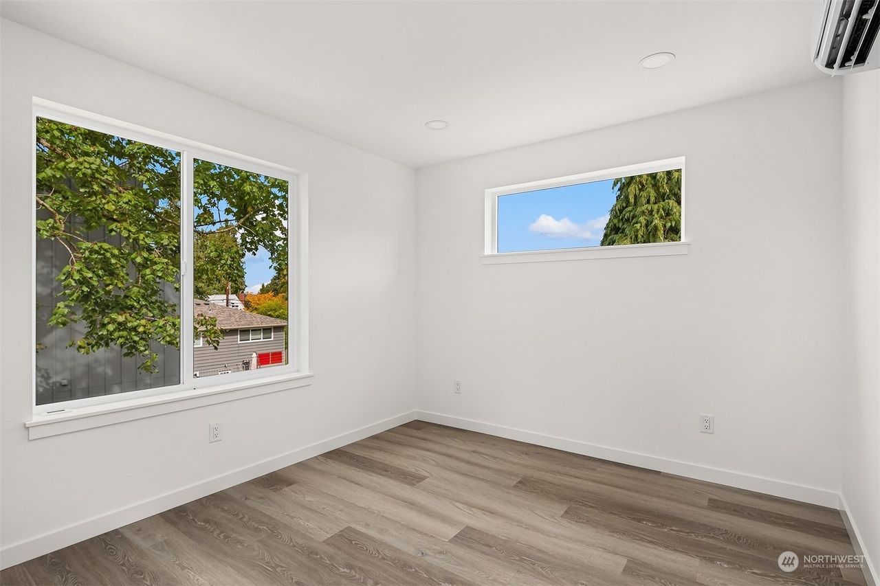Empty white bedroom with large windows and light wood flooring, showing trees outside