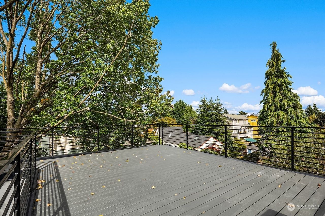 Wooden deck with black railing overlooking trees, blue sky, and a suburban neighborhood
