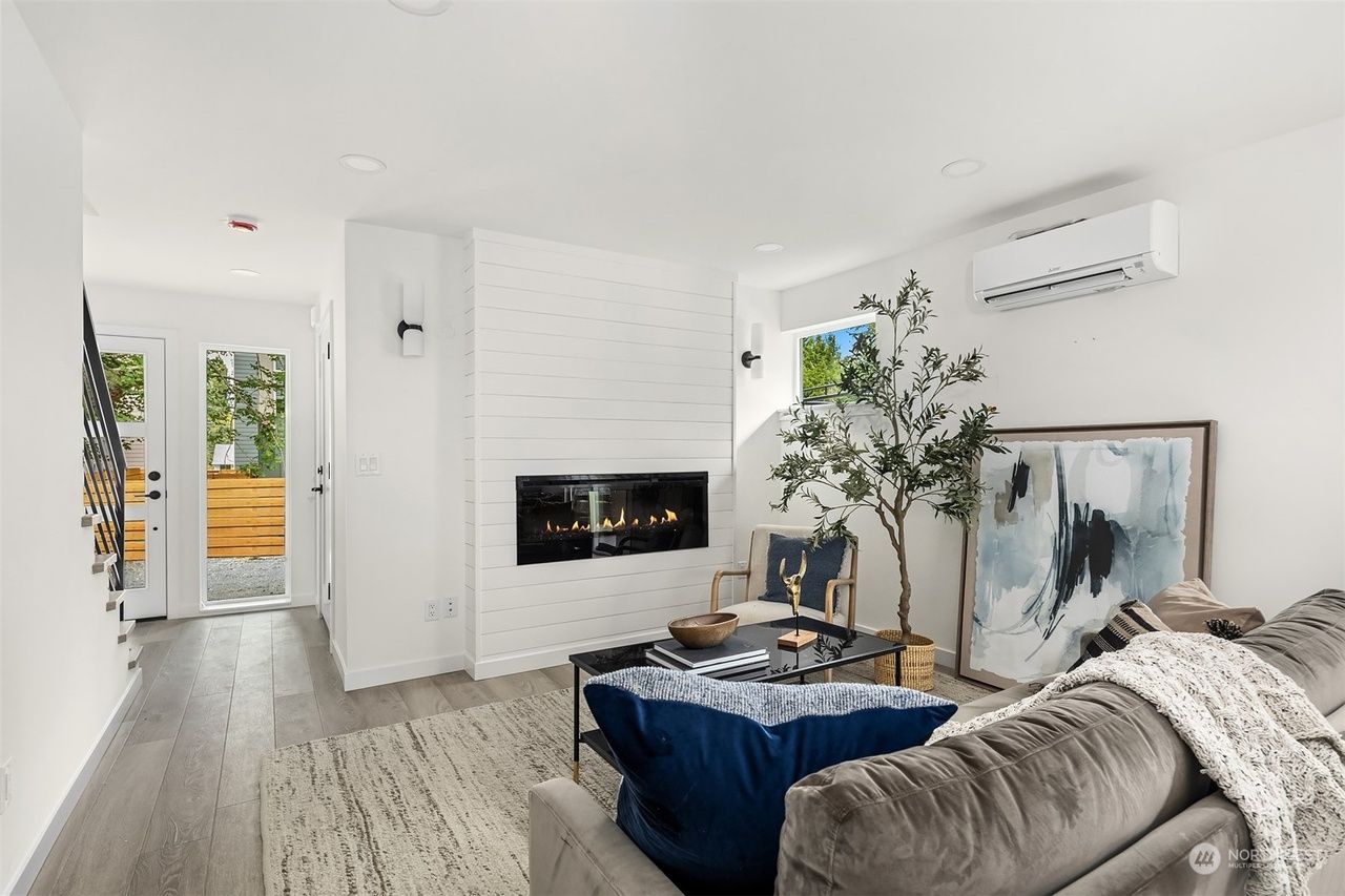 Modern white living room with a fireplace, blue sofa, indoor plant, and artwork near a balcony door