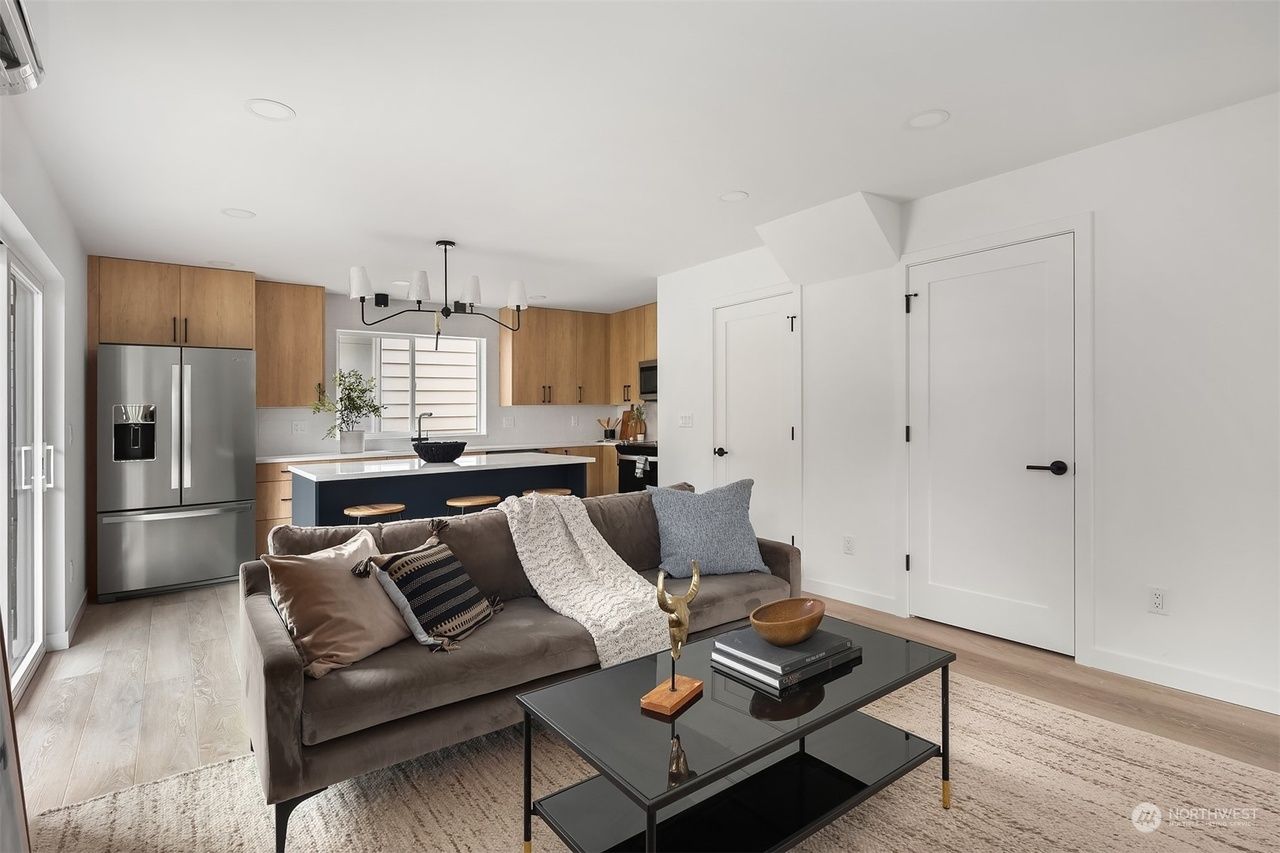 Modern open-plan living room with brown sofa, black coffee table, kitchen, and stainless steel fridge