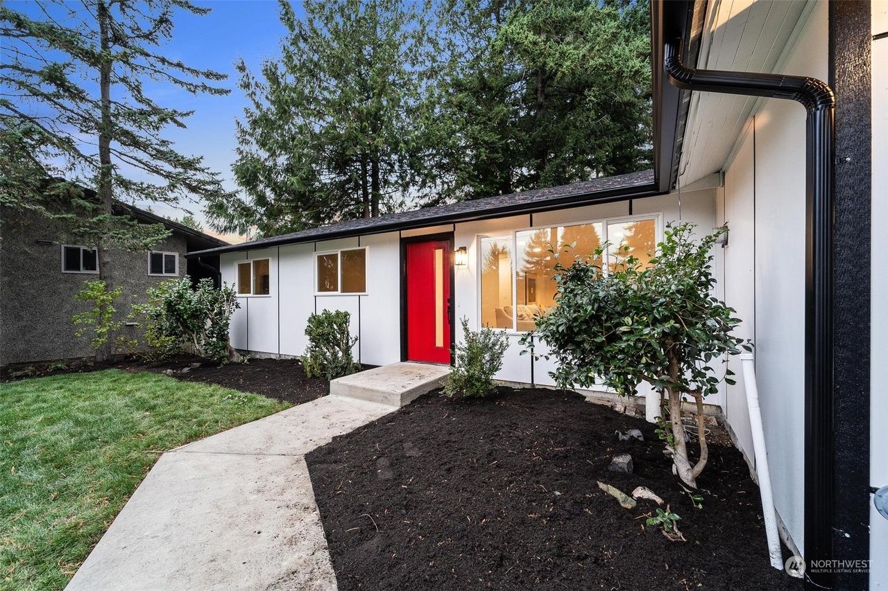 Front entry of a white house with a red door, curved walkway, and landscaped front yard