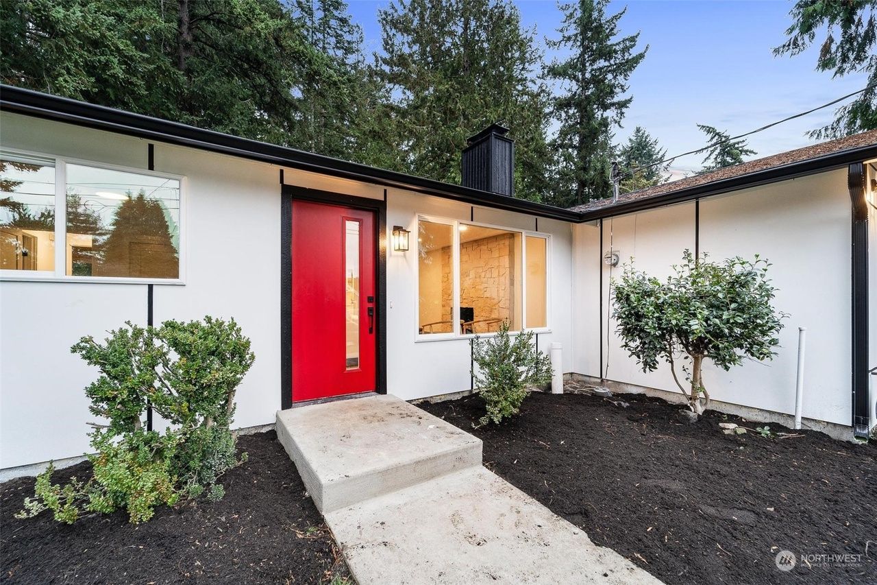 Modern house exterior with a red front door, concrete walkway, and landscaped shrubs