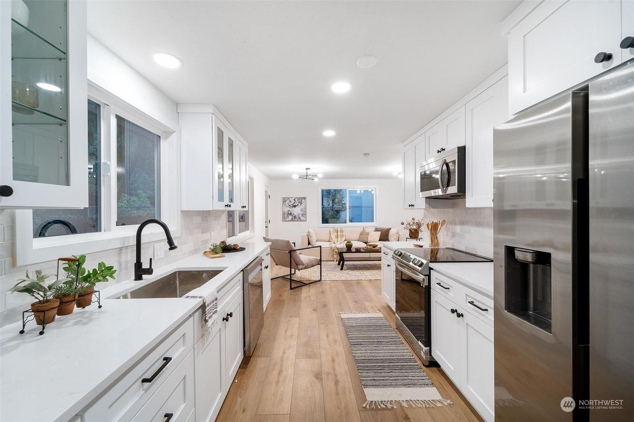 Bright white galley kitchen with stainless steel appliances and wood floor leading to a cozy dining nook.