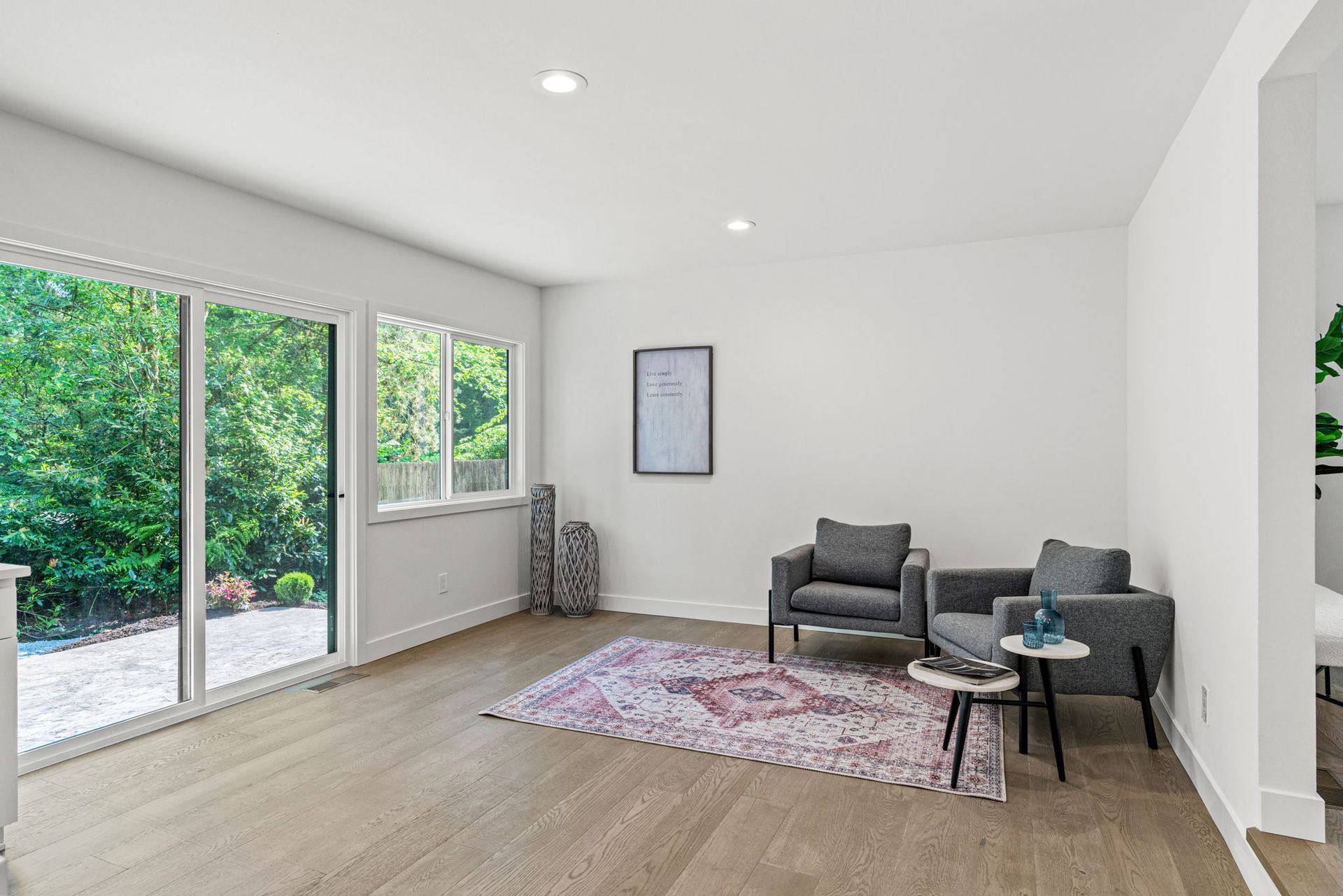 Bright modern living room with gray chairs, pink rug, small table, and large sliding glass doors to a garden
