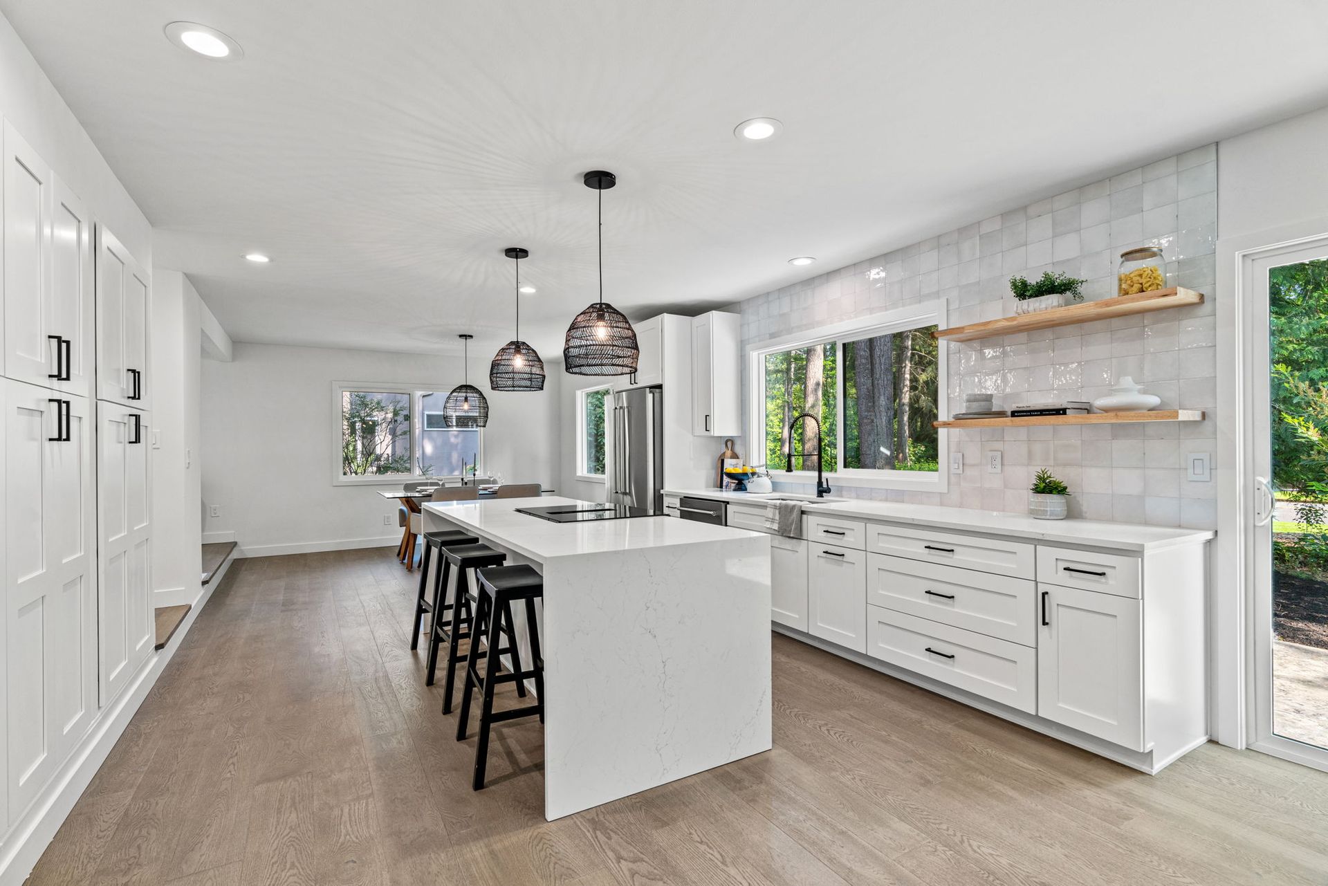 Bright modern kitchen with white cabinets, island seating, and large windows.