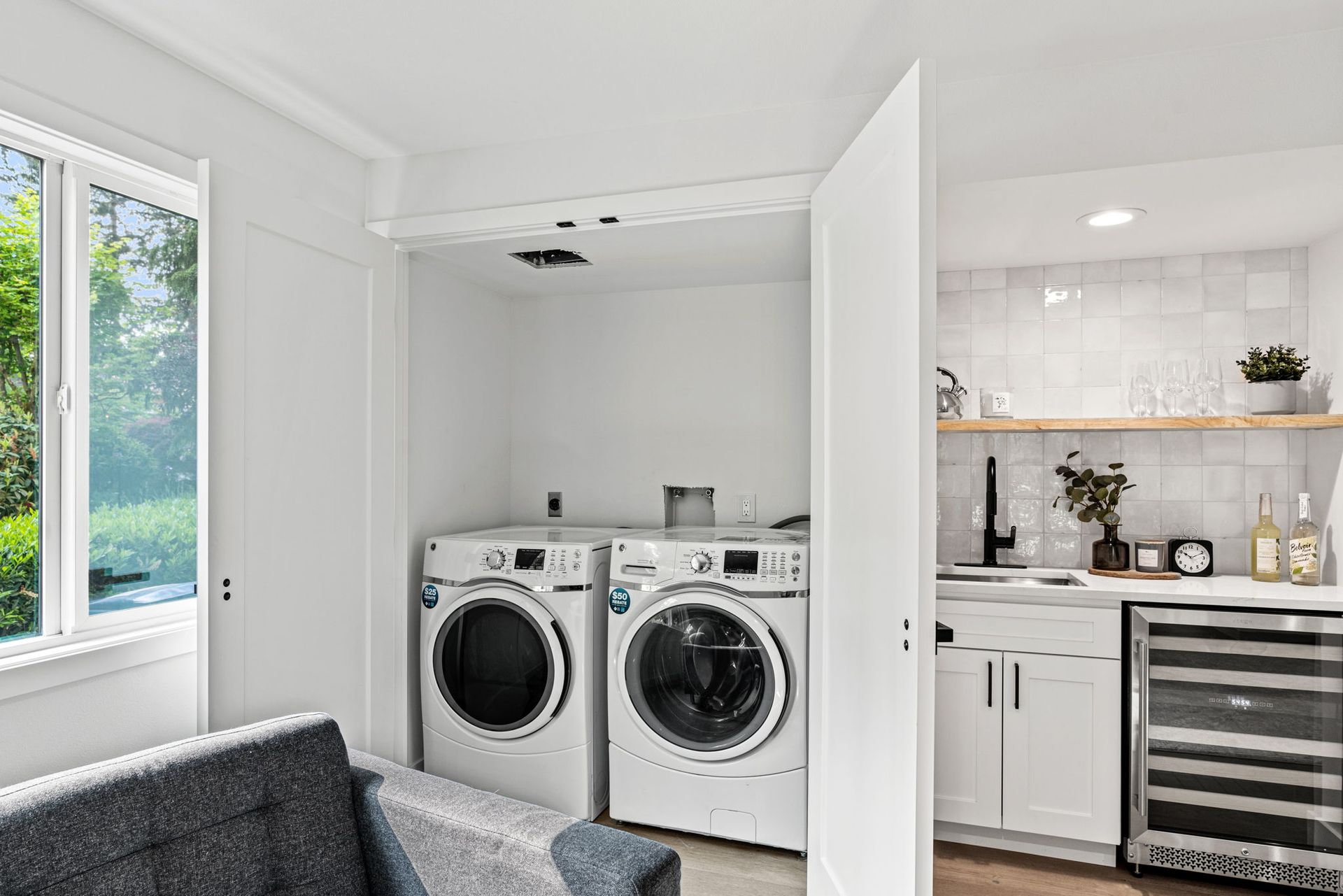 Modern laundry nook with front-load washer and dryer beside a bright white kitchen with open shelves.