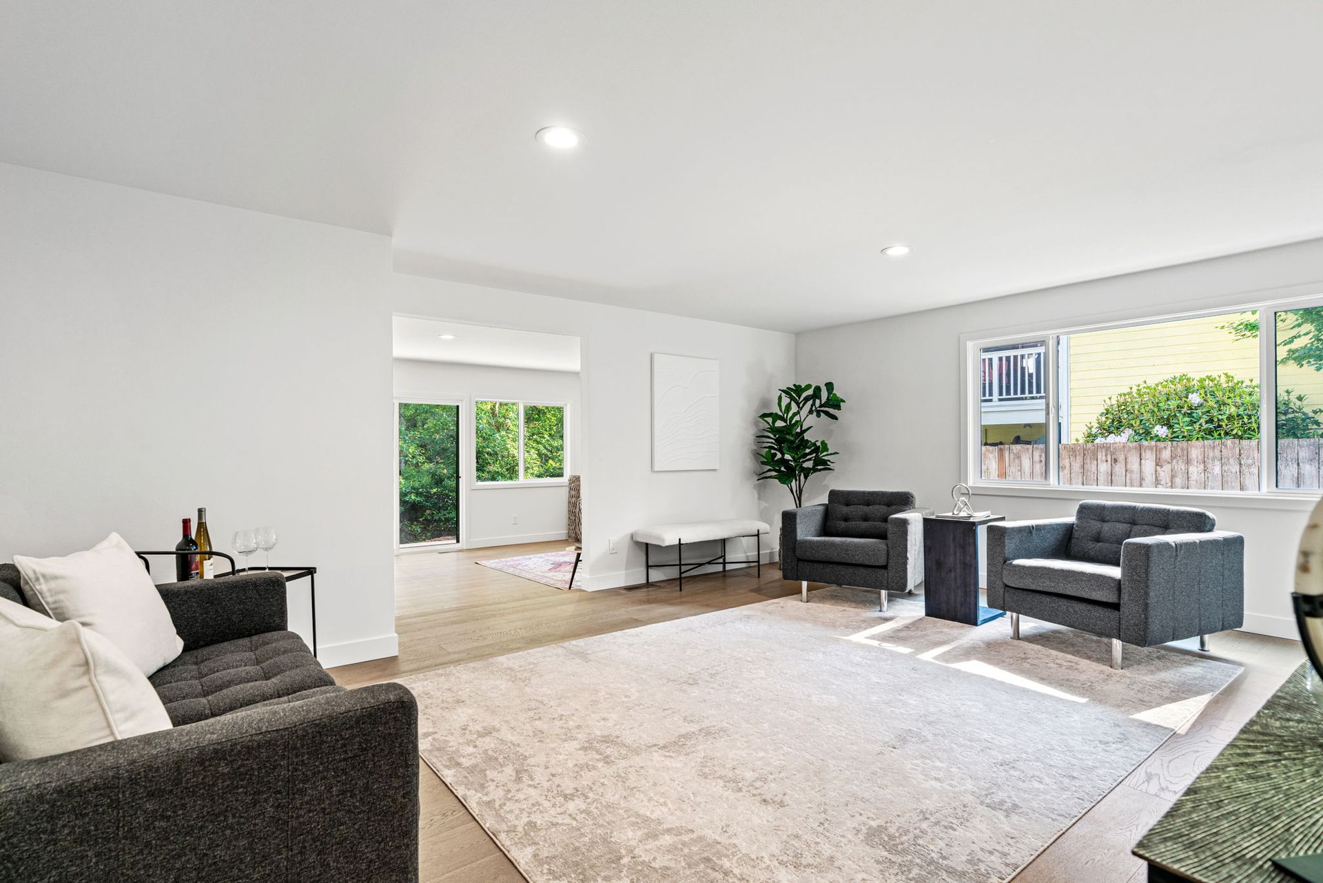 Bright modern living room with gray sofas, cream rug, large windows, and white walls.