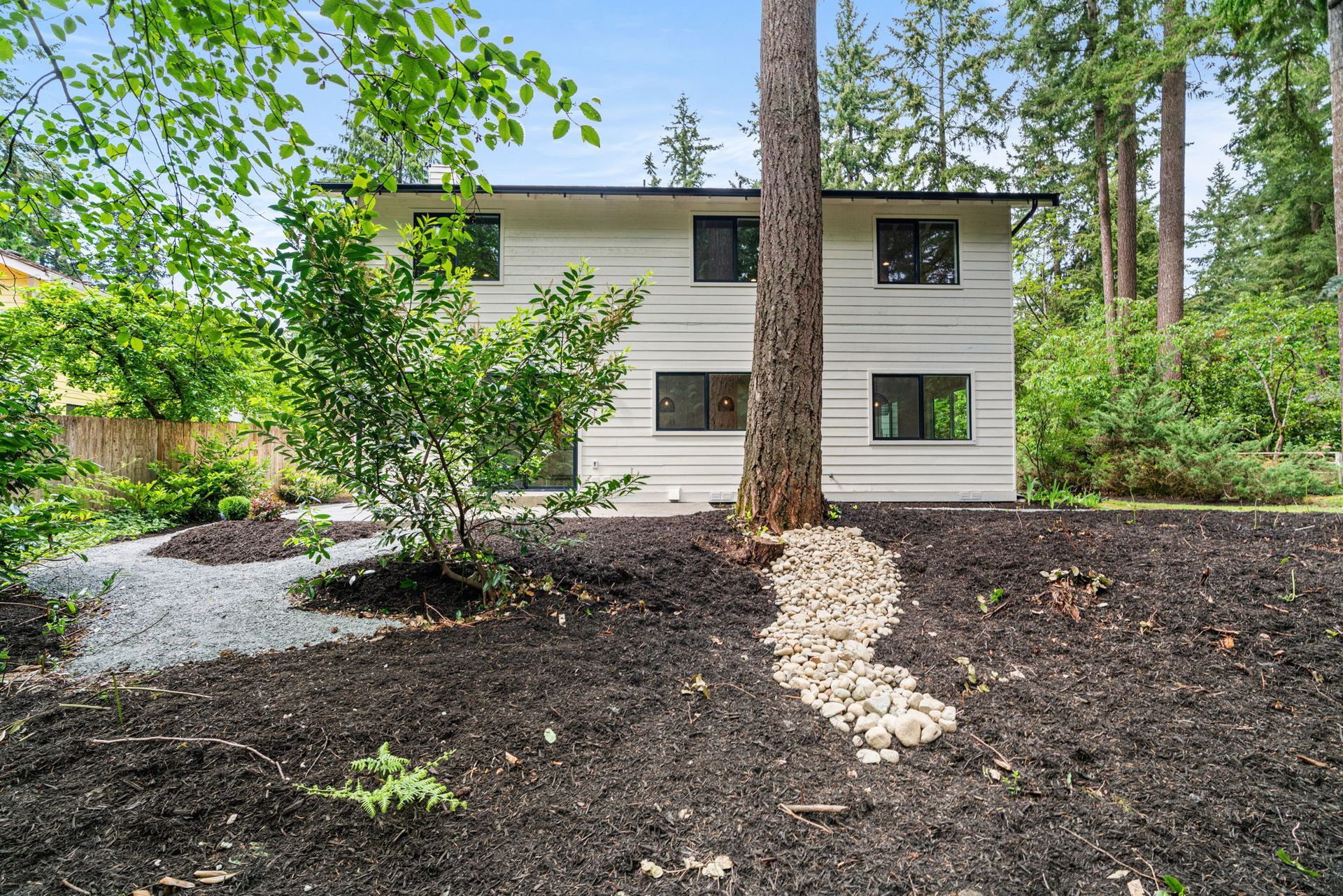 Modern two-story house with gray siding, surrounded by trees and a mulched front yard.