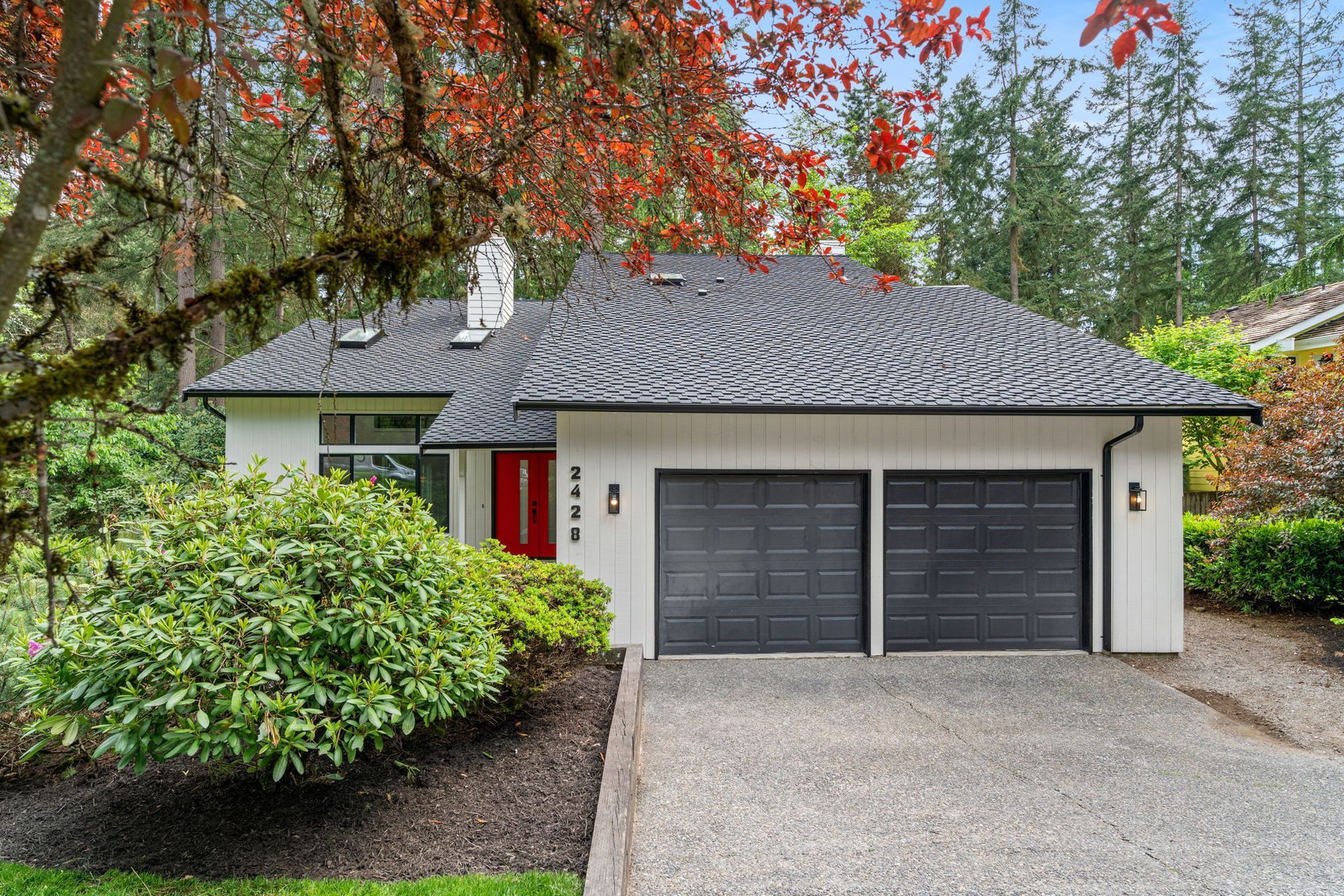Suburban house with gray roof, double garage, red front door, and leafy trees in front yard