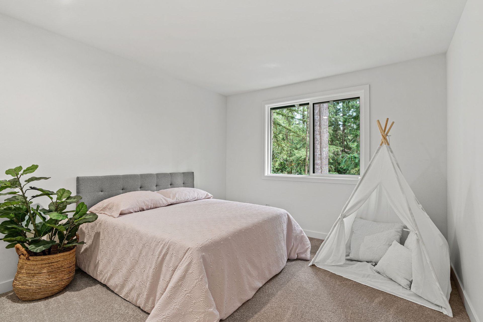 Bright minimalist bedroom with gray bed, white teepee, plant, and window view of trees
