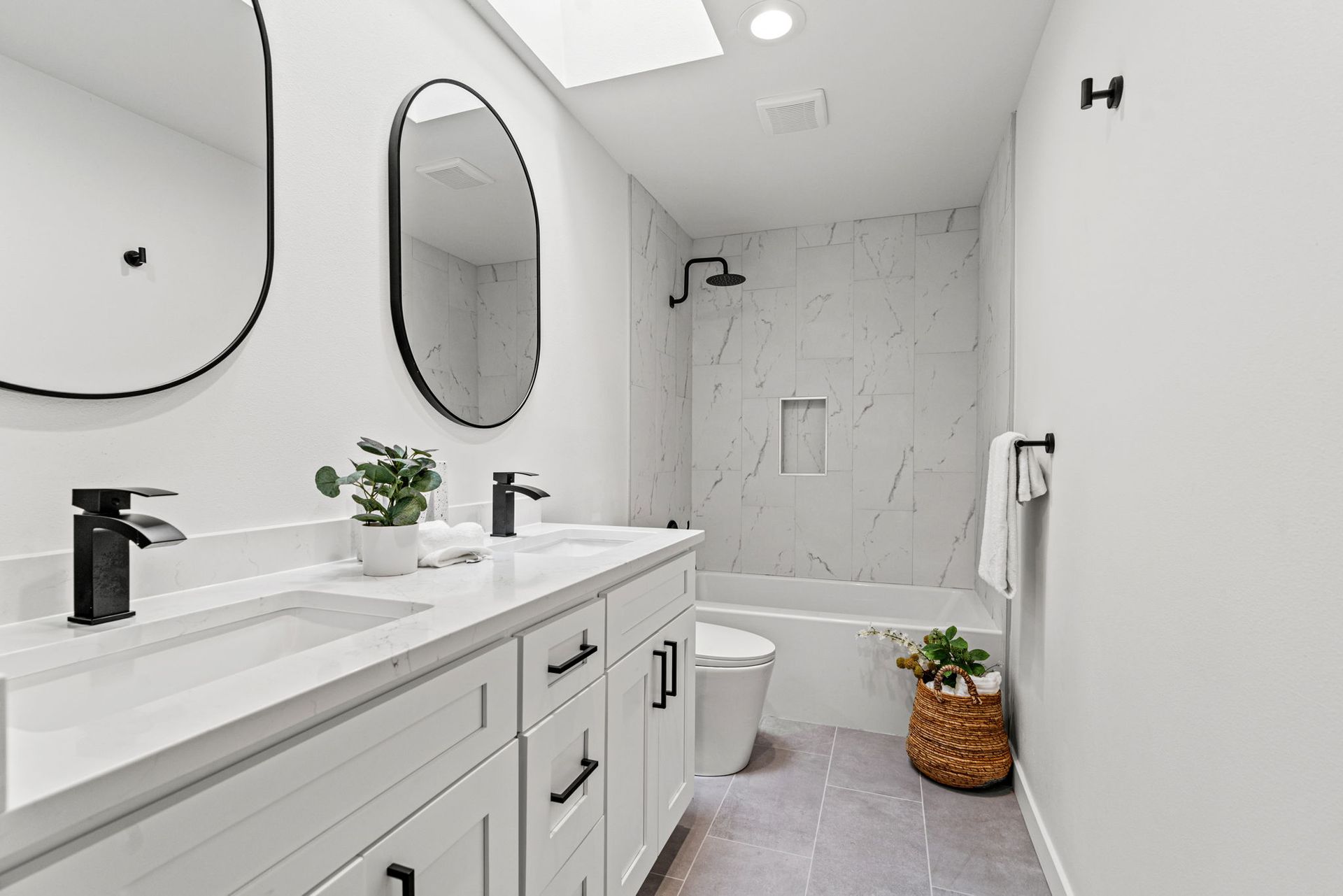 Bright white bathroom with double vanity, oval mirrors, and marble shower walls