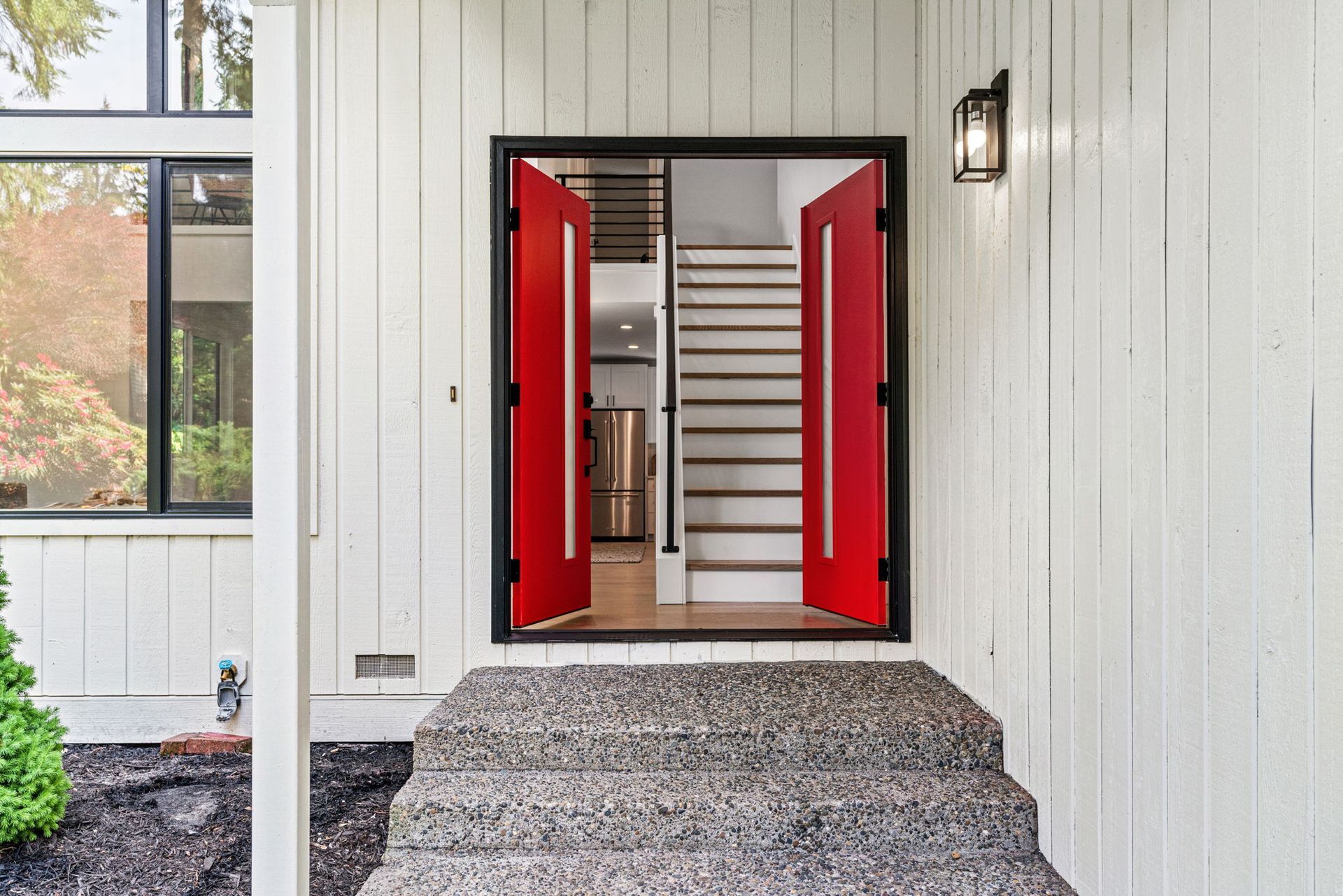 Open red double doors leading to a stairway, at a house entrance with white siding.